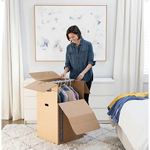 Woman packing clothes into a wardrobe box in a bedroom.